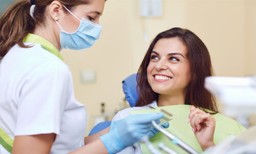 Close-up picture of a smiling woman with short brown hair, looking at a dental assistant, showing her happiness with the Holistic bonding procedure she had done at Premier Holistic Dental in beautiful Costa Rica.