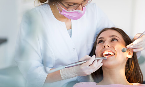 Close –up picture of a woman with long blonde hair and perfect teeth, smiling and showing her happiness with the crown lengthening procedure she had in Costa Rica.