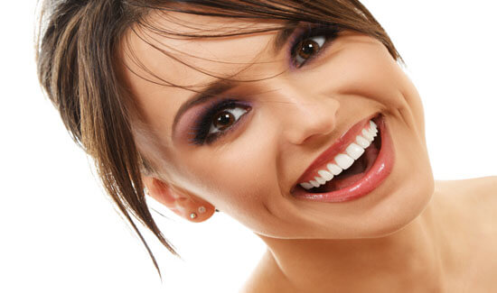 Close-up picture of a smiling woman with short brown hair and perfect teeth, tilting her head while looking directly at the camera, and showing her happiness with the all-on-four dental treatment she had at Premier Holistic Dental in beautiful Costa Rica.