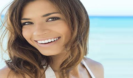 Portrait picture of a smiling woman with long brown hair and perfect teeth, looking at the camera and showing her happiness with the dental fillings she had in Costa Rica.
