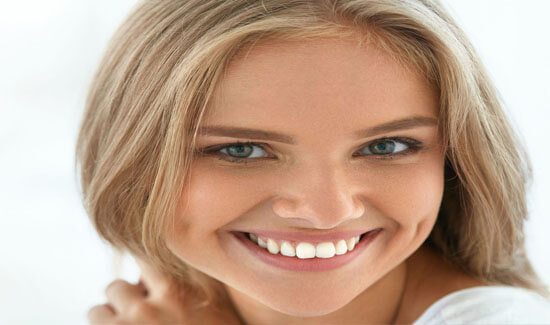 Close-up picture of a smiling woman with long blonde hair and perfect teeth, looking directly at the camera and showing her happiness with the Huggins-Grube Protocol procedure she had at Premier Holistic Dental in beautiful Costa Rica.