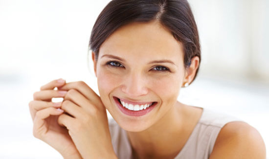 Close-up picture of a smiling woman with short dark hair and perfect teeth, looking directly at the camera and showing her happiness with the implant-supported dentures procedure she had at Premier Holistic Dental in beautiful Costa Rica.