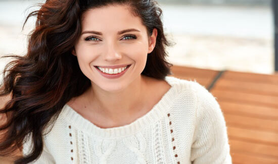 Close-up portrait picture of a smiling woman with long brown hair and with perfect teeth, looking directly at the camera and showing her happiness with the prp procedure she had at Premier Holistic Dental in beautiful Costa Rica.