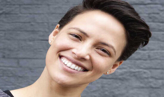 Close-up portrait picture of a smiling woman with short dark hair and perfect teeth, illustrating her happiness with the root canals treatment she had at Premier Holistic Dental in beautiful Costa Rica.