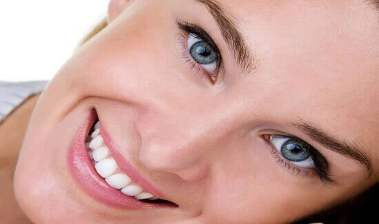 Close-up portrait picture of a smiling woman with short hair and with perfect teeth, resting her head on her hand, showing her happiness with the dental veneers she had at Premier Holistic Dental in beautiful Costa Rica.