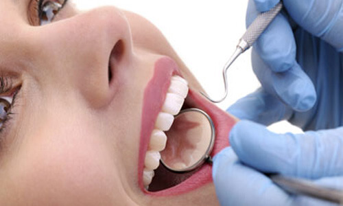 Close-up picture of a smiling woman with perfect teeth showing her happiness with the dental bridge she received at Premier Holistic Dental in beautiful Costa Rica.  The picture shows a dentist with dental utensils in her mouth showing how the procedure is done.