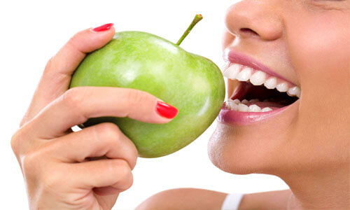 Close-up picture of a smiling woman, biting into a green apple, showing her perfect teeth, and happy with the endodontics dental work she had done at Premier Holistic Dental in beautiful Costa Rica.