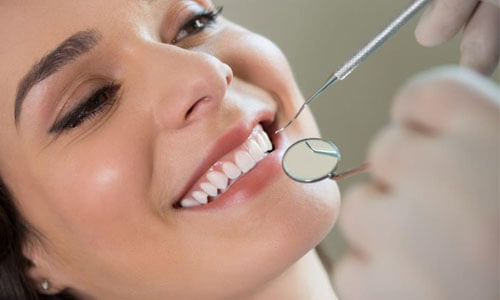 Close up picture of a smiling woman with white perfect teeth in a dental chair showing her happiness with the dental full mouth makeover she received at Premier Holistic Dental in beautiful Costa Rica.  A dentist is holding dental tools showing how the procedure is done.