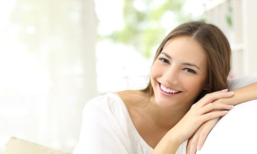Close-up picture of a smiling woman with long brown hair and wearing a white blouse, showing her happiness with the Huggins-Grube Protocol procedure she had done at Premier Holistic Dental in beautiful Costa Rica.