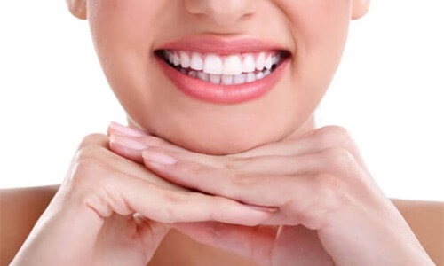 Close up picture of a smiling woman with both hands under her chin, with white perfect teeth, showing her happiness with the implant supported bridge she received at Premier Holistic Dental in beautiful Costa Rica.