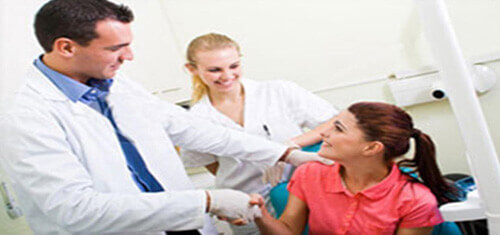 Picture of a smiling patient in a dental chair and having holistic dental work in Costa Rica. The picture also shows a dentist and dental assistant in white coats.