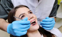 Picture of a smiling woman in a dental chair having a Prosthodontics dental treatment by Premier Holistic Dental in beautiful Costa Rica.  The dentist has blue gloves and dental tools and is performing the treatment.