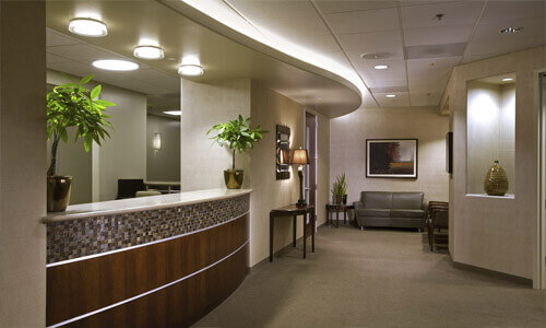 Picture of a dental office reception area.  The picture shows warm beige colors and a well-lighted plush interior.