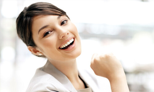 Close-up picture of a smiling woman with short brown hair and perfect white teeth, looking into the camera,, and showing her happiness with the Holistic dental implants she had done at Premier Holistic Dental in beautiful Costa Rica.